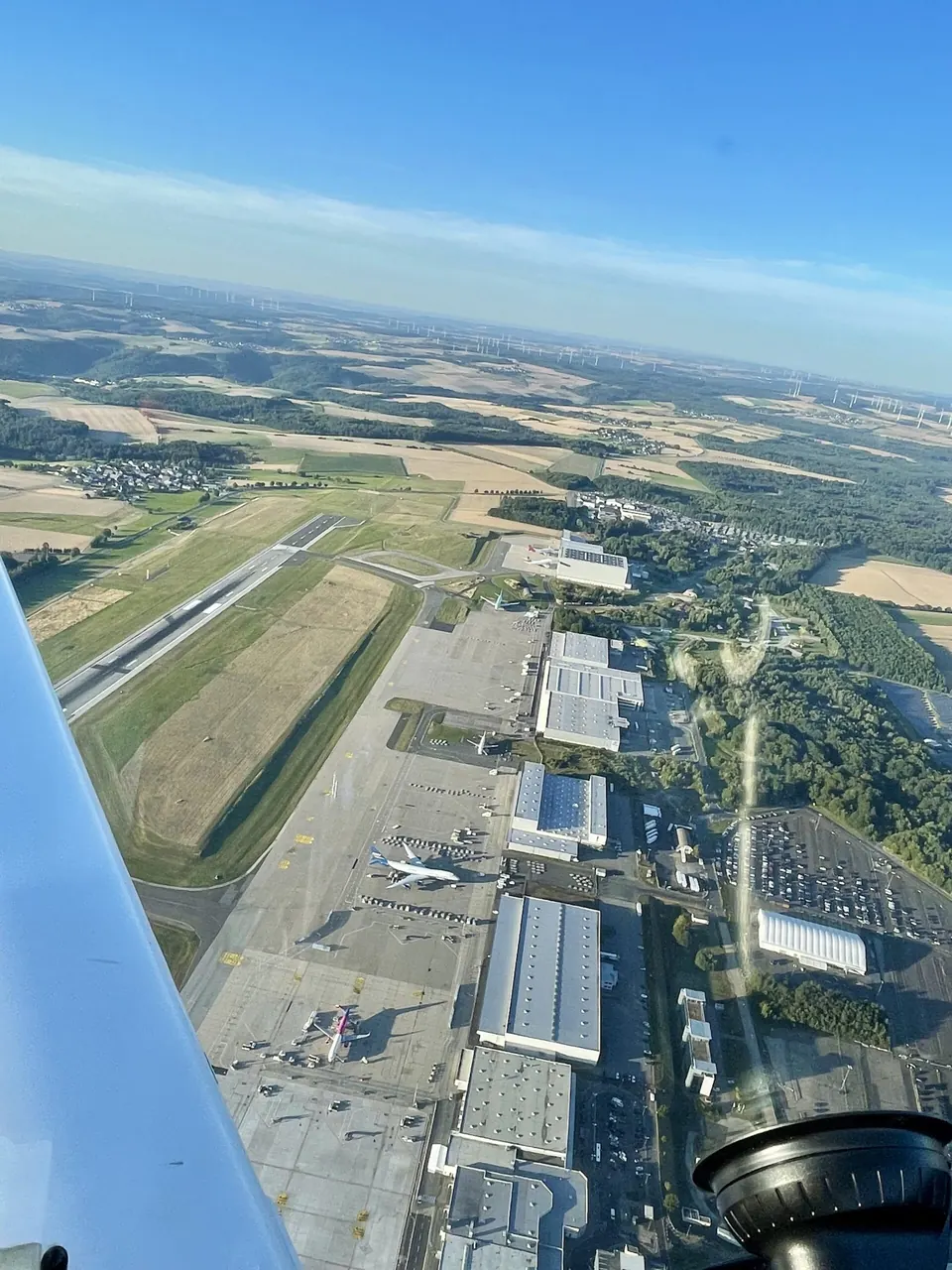Luftbild eines Flugplatzes mit Piste und Hallen aus dem Cockpit