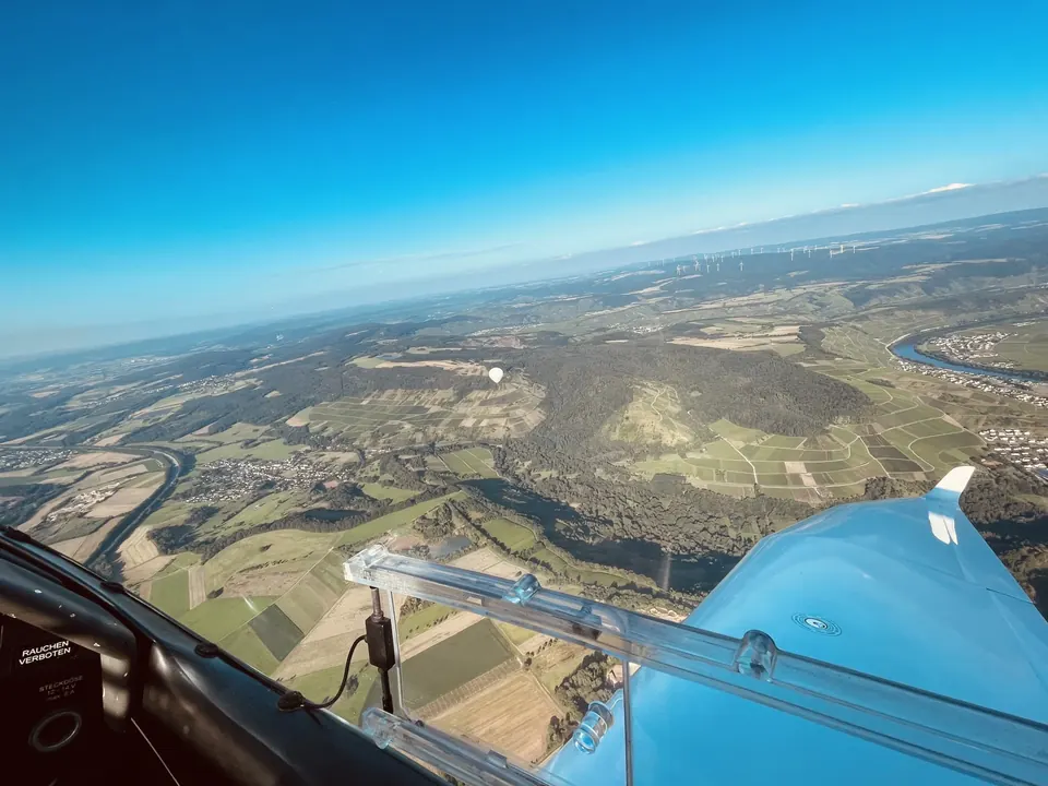 Blick aus dem Cockpit über die Tragfläche auf Hügel, Felder und die Saarschleife im Gegenlicht