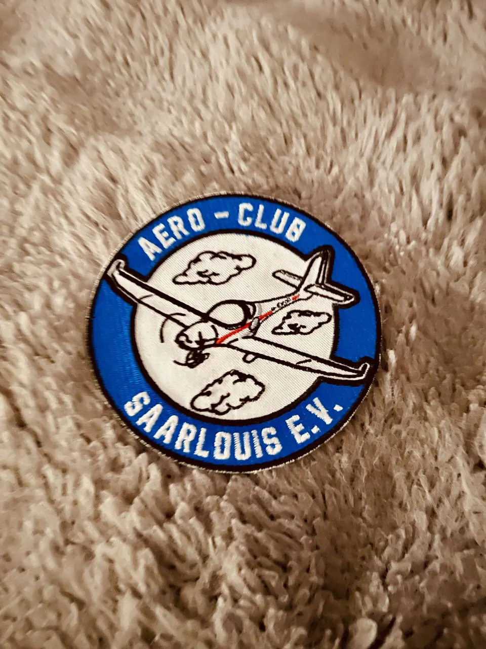 Anstecker mit blauem Vereinslogo des Aero-Club Saarlouis auf Fell