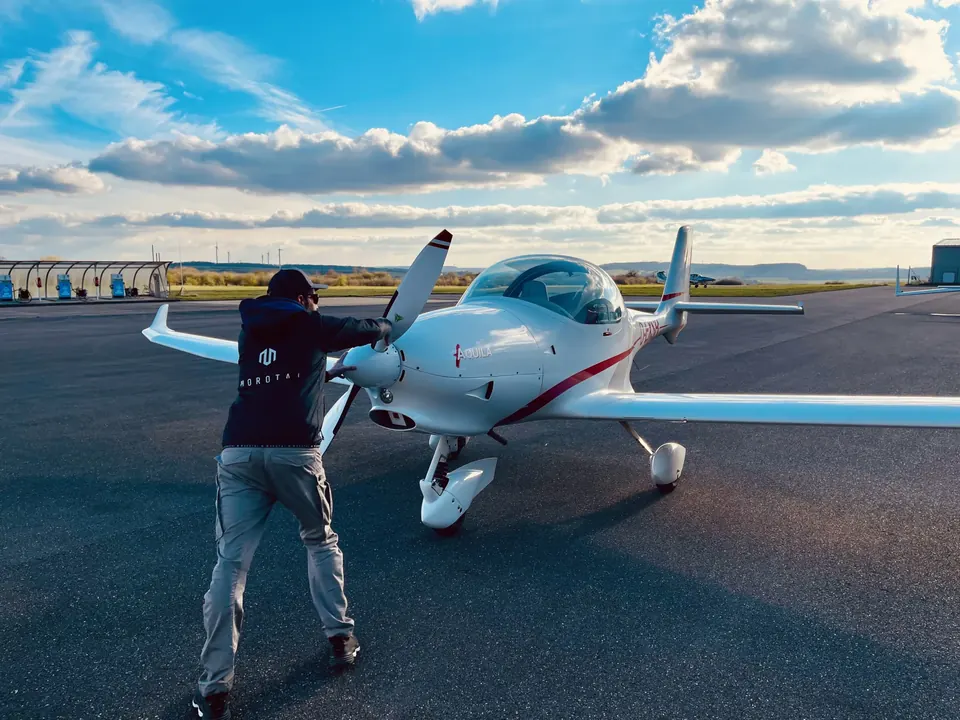 Fluglehrer beim Außencheck an der Aquila A210 vor Wolkenhimmel