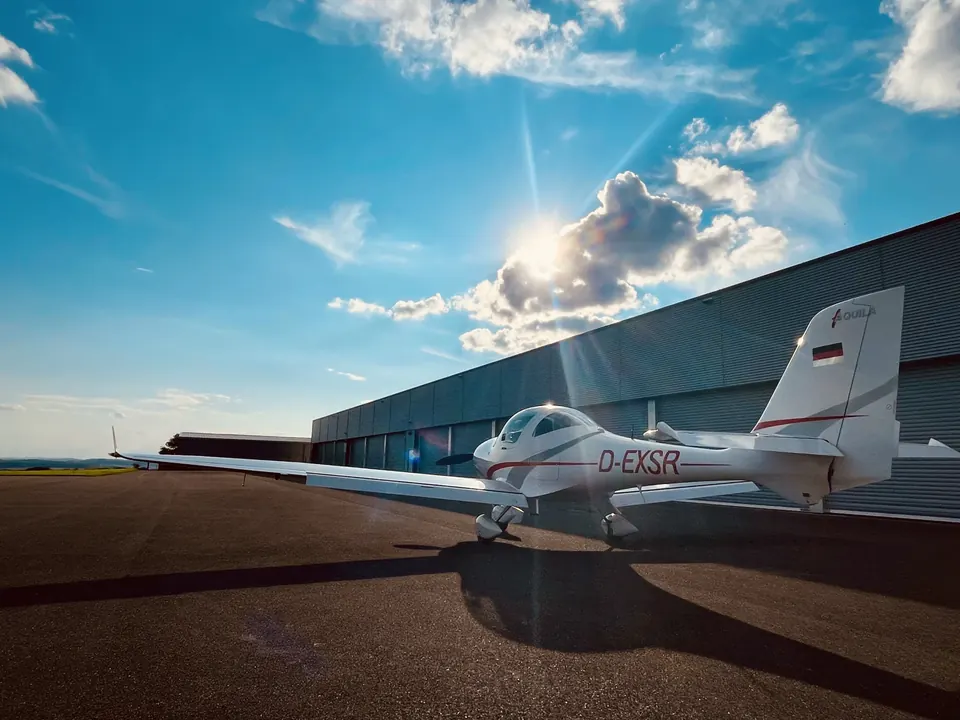 Aquila A210 D-EXSR vor dem Hangar am Flugplatz Saarlouis-Düren, Sonne bricht durch die Wolken