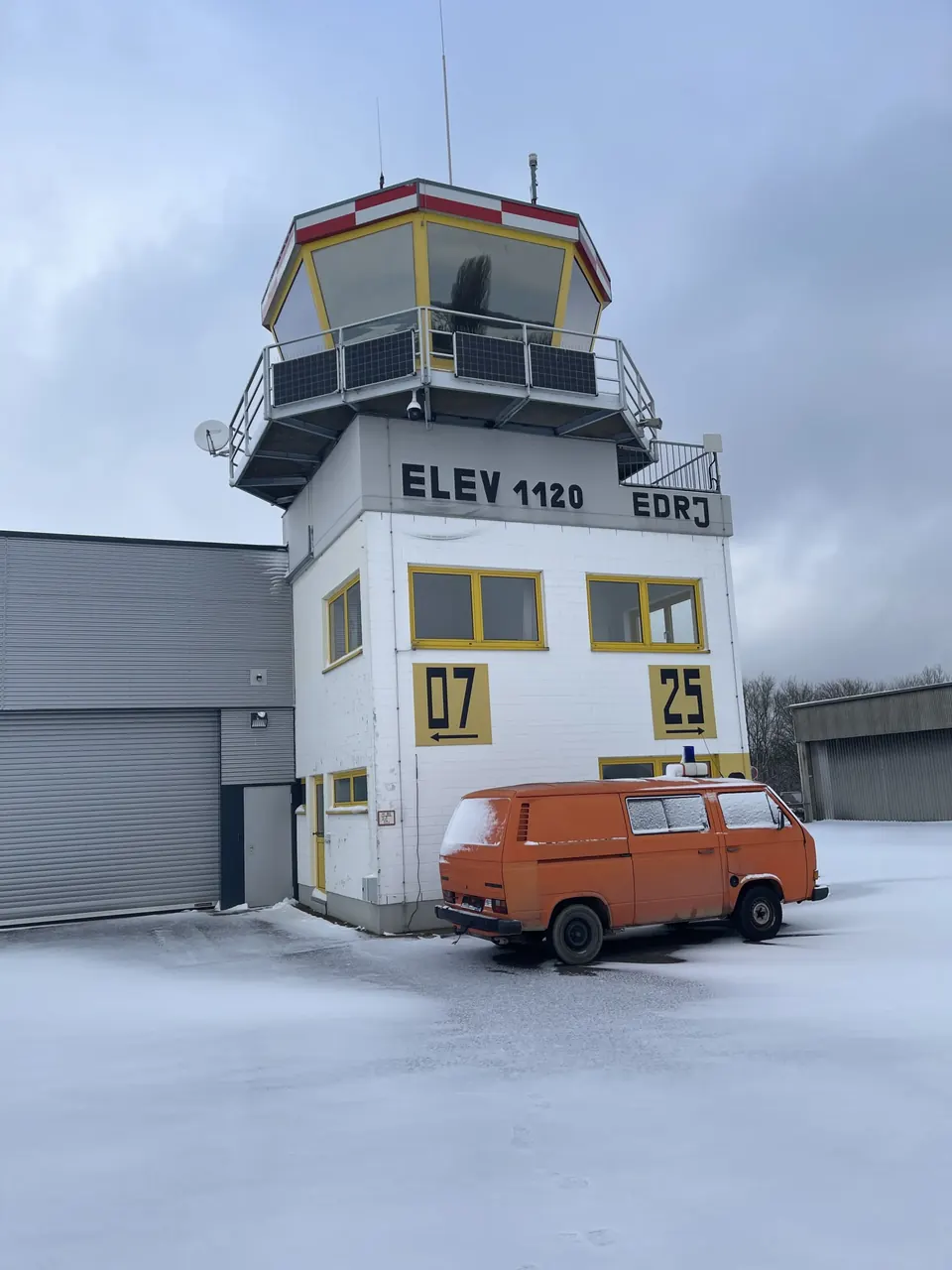 Tower des Flugplatzes Saarlouis-Düren im Schnee mit Pistenbezeichnung 07 und 25 und orangem Bulli davor